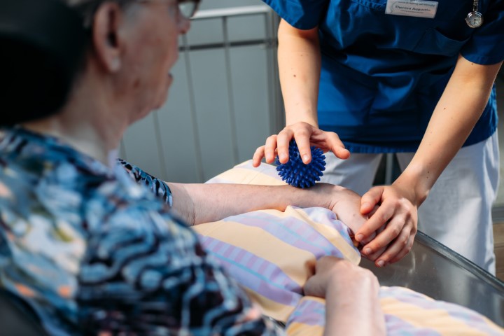 Eine Pflegekraft führt eine aktivierende basale Stimulation auf dem Arm bei einer Patientin im Wachkoma durch.