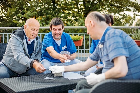 Ein Pfleger spielt mit Patienten Karten in der außerklinischen Intensivpflege in Hamburg.