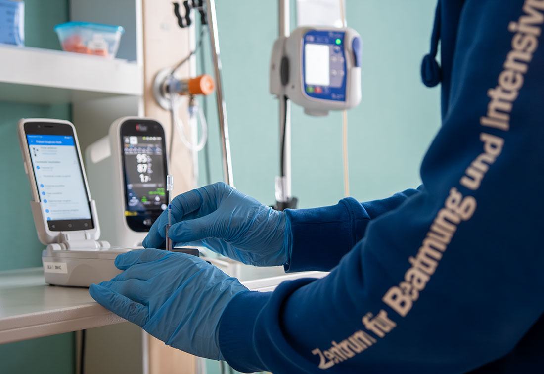 Eine Pflegefachkraft arbeitet in einem Patientenzimmer am Blutgasanalyse-Gerät in Großaufnahme