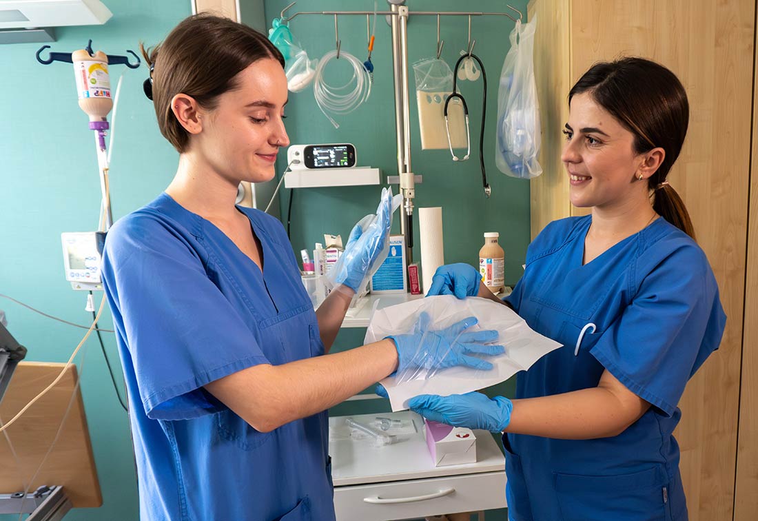Eine Fachpflegekraft unterstützt eine Auszubildende beim Anlegen eines sterilen Handschuhs